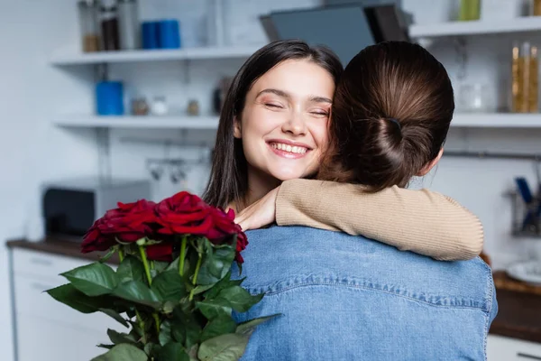 Compiaciuta giovane donna che abbraccia l'uomo ad occhi chiusi mentre tiene in mano mazzo di rose a casa — Foto stock