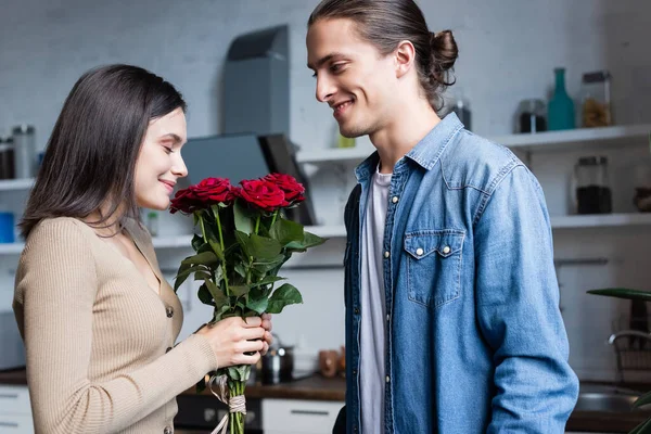 Pleased woman holding bouquet of roses with closed eyes near young man — Stock Photo