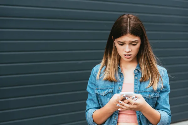 Adolescente trastornado usando teléfono inteligente cerca del edificio al aire libre - foto de stock