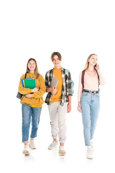 Adolescentes sonrientes con mochilas, cuadernos y teléfonos inteligentes caminando sobre fondo blanco - foto de stock