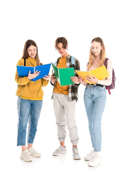 Adolescentes sonrientes con mochilas mirando libros de texto sobre fondo blanco - foto de stock