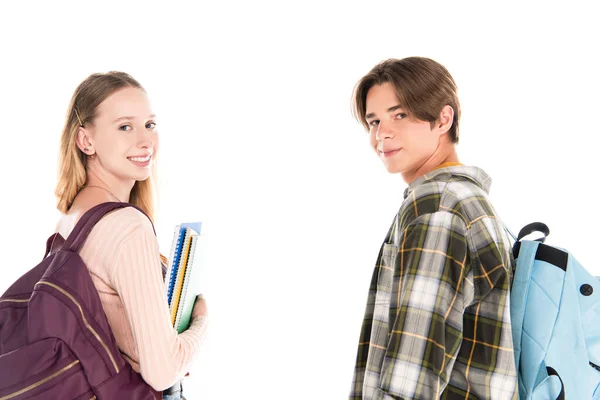 Adolescentes amigos sonriendo a la cámara mientras sostienen mochilas y cuadernos aislados en blanco - foto de stock