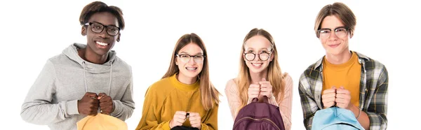 Панорамний знімок багатоетнічних підлітків в окулярах тримає рюкзаки і посміхається ізольовано на білому — стокове фото