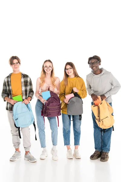 Cheerful multicultural teenagers with books and backpacks looking at camera on white background — Stock Photo