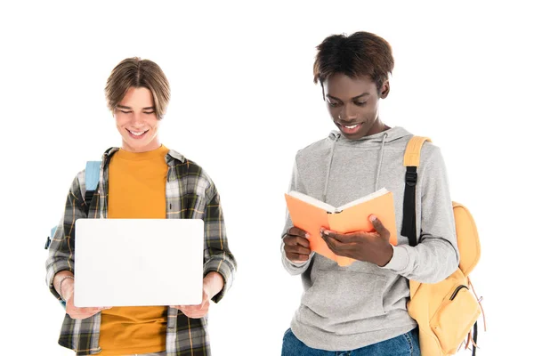 Smiling multiethnic teenagers with book and laptop isolated on white — Stock Photo