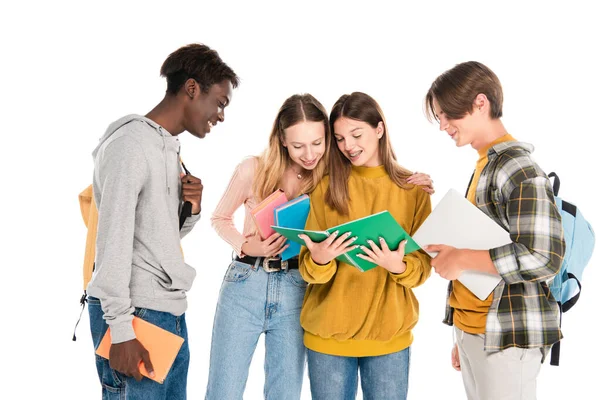 Positive multikulturelle Teenager mit Büchern und Laptop, die sich das Kopierbuch isoliert auf Weiß ansehen — Stockfoto