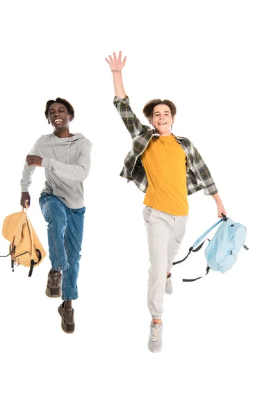 Alegre multiétnicos adolescentes con mochilas saltando aislados en blanco - foto de stock