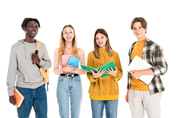 Multiethnische Teenager mit Büchern und Laptop lächeln isoliert auf weiß in die Kamera — Stockfoto