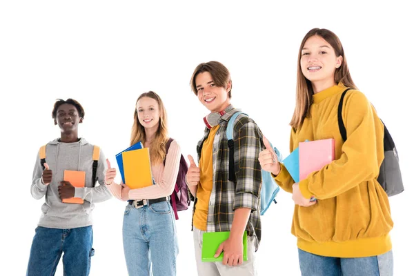 Adolescentes multiculturais sorridentes com mochilas e livros mostrando como isolado no branco — Fotografia de Stock