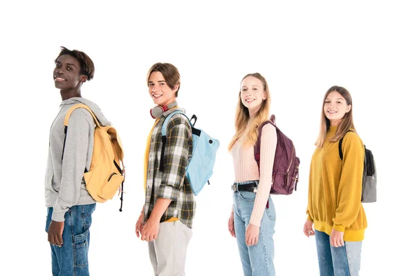 Adolescenti multietnici sorridenti con zaini che guardano la fotocamera isolata sul bianco — Foto stock