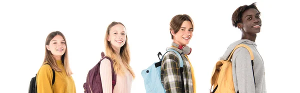 Заголовок сайта улыбающихся мультикультурных подростков с рюкзаками, смотрящих на камеру, изолированную на белом — стоковое фото