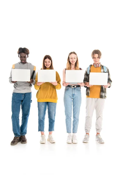 Adolescents multiethniques souriants avec des sacs à dos tenant des ordinateurs portables sur fond blanc — Photo de stock
