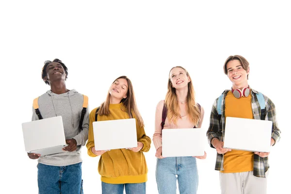 Adolescentes multiculturales positivos con computadoras portátiles y mochilas aisladas en blanco - foto de stock