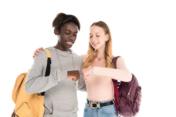 Smiling teenager with backpack doing fists bump with african american friend isolated on white — Stock Photo