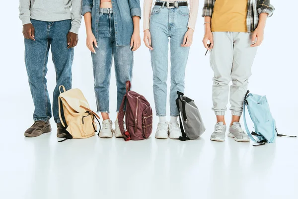 Vista cortada de adolescentes multiétnicos em pé perto de mochilas em fundo cinza — Fotografia de Stock