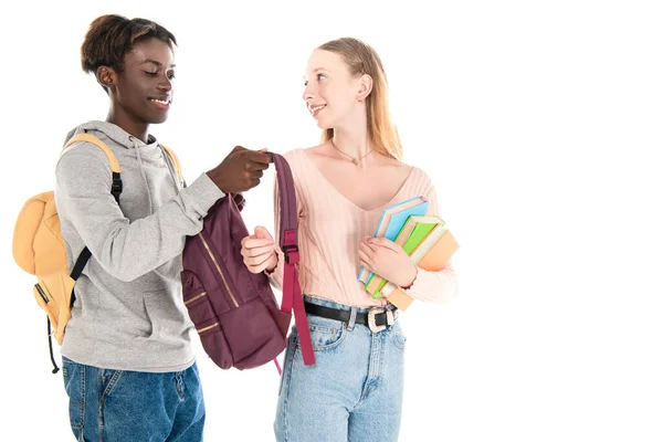 Smiling african american teenager holding backpack near girl with books isolated on white — Stock Photo
