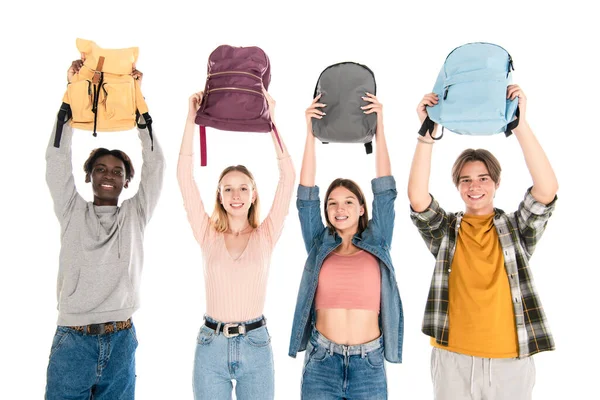 Alegre multicultural adolescentes sosteniendo mochilas y mirando a la cámara aislada en blanco - foto de stock