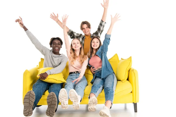 Positive multicultural teenagers waving hands and looking at camera on sofa on white background — Stock Photo