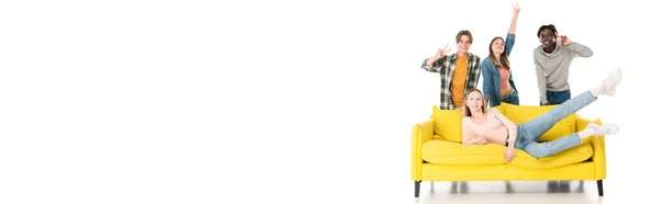 Panoramic shot of cheerful multiethnic teenagers showing peace sign near yellow couch on white background — Stock Photo