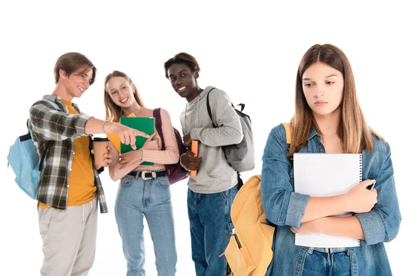 Enfoque selectivo de adolescentes multiétnicos sonriendo cerca de chica triste con cuaderno aislado en blanco - foto de stock
