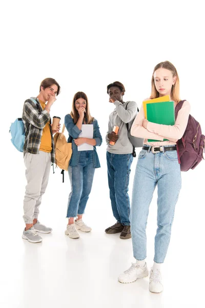 Chica triste con cuadernos de pie cerca sonriendo adolescentes multiétnicos sobre fondo blanco - foto de stock