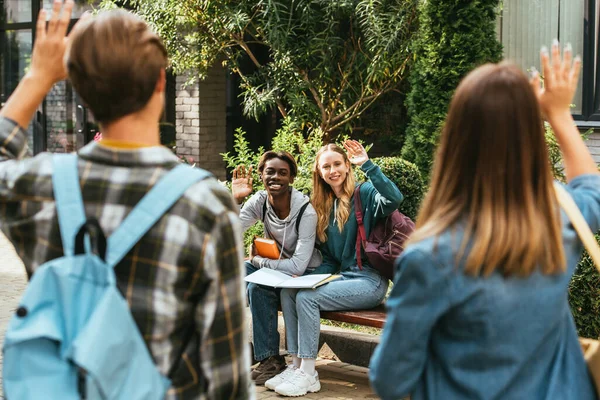 Focus selettivo di adolescenti multiculturali con zaini che salutano all'aperto — Foto stock