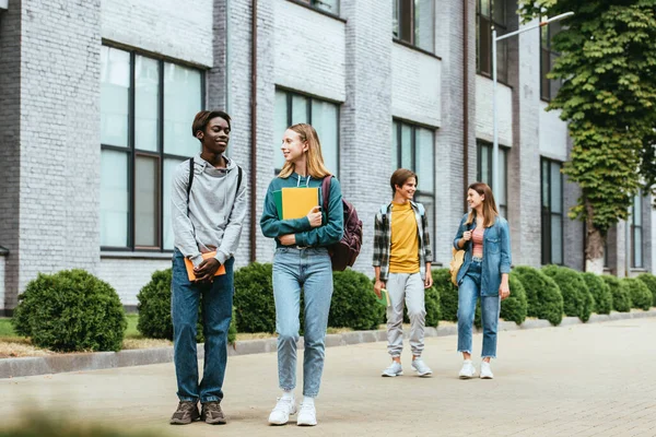 Selektiver Fokus eines afrikanisch-amerikanischen Teenagers mit einem Buch, das in der Nähe eines Freundes auf einer städtischen Straße läuft — Stockfoto