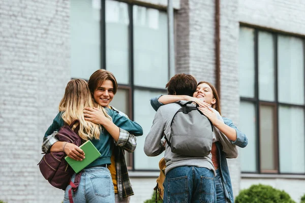 Adolescentes multiculturais sorridentes com mochilas abraçando ao ar livre — Fotografia de Stock
