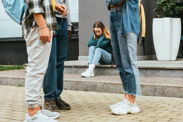 Foco seletivo de menina chateada sentado perto de adolescentes multiétnicos ao ar livre — Fotografia de Stock