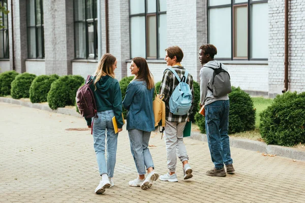 Back view of smiling teenagers with backpacks walking on urban street — Stock Photo