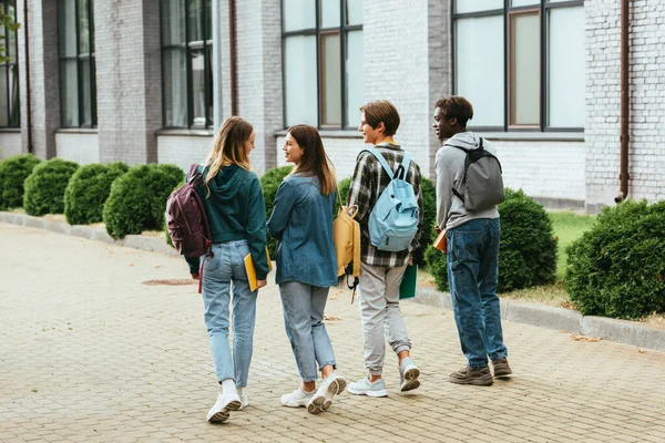 Vista posteriore di adolescenti sorridenti con zaini che camminano per strada urbana — Foto stock