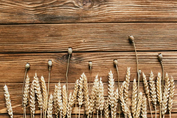 Vista dall'alto di papaveri secchi e spighe di grano su sfondo di legno — Foto stock