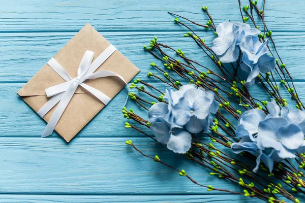 Ansicht von oben auf blauem Holzgrund mit blühenden Zweigen und Blumen in der Nähe von Briefumschlag — Stockfoto