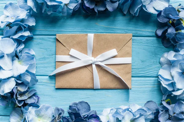 Top view of wooden blue background with floral frame around envelope — Stock Photo