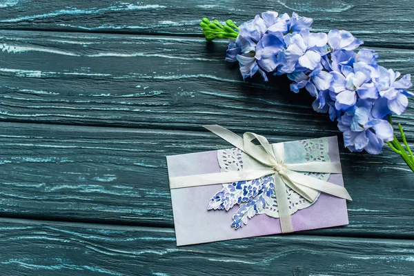 Вид зверху на дерев'яний зелений фон з синіми квітами та конвертом — Stock Photo