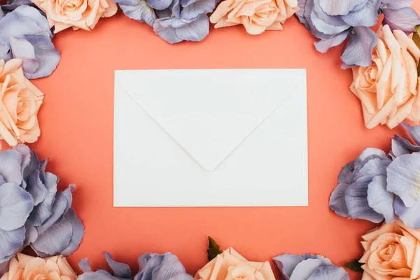 Top view of white envelope and floral frame on coral background — Stock Photo