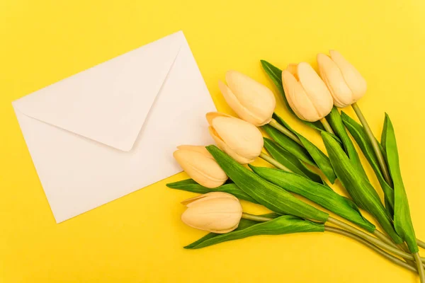 Верхний вид конверта рядом с тюльпанами на желтом фоне — стоковое фото