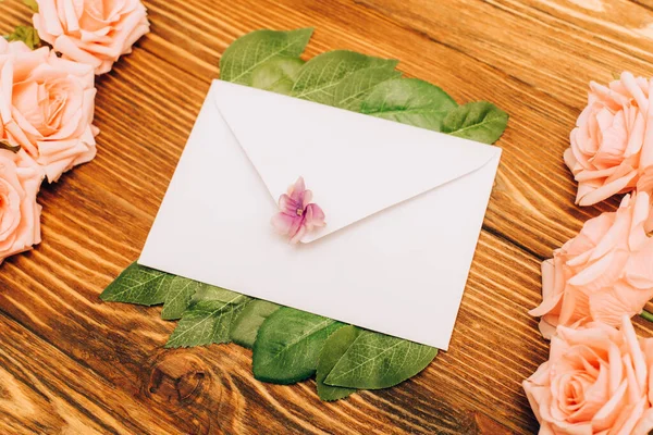 Верхний вид конверта рядом с розами на деревянном фоне — стоковое фото