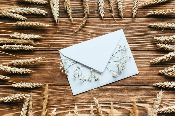 Vue de dessus de l'enveloppe avec des fleurs sauvages sèches sur fond en bois avec cadre de blé — Photo de stock