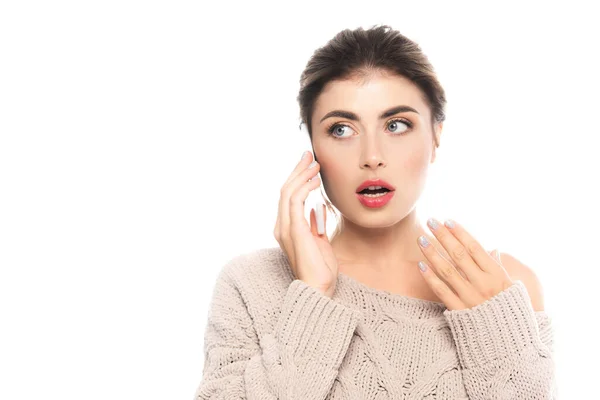 Здивована жінка в модному в'язаному светрі говорить на смартфоні, тримаючи руку біля обличчя ізольовано на білому — стокове фото