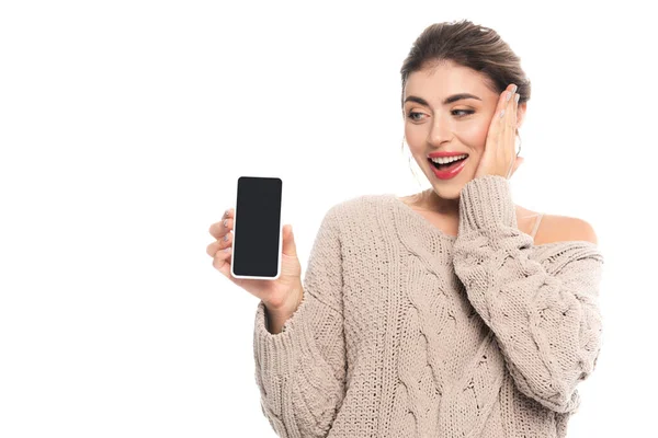 Mujer sorprendida sosteniendo teléfono inteligente con pantalla en blanco mientras toca la cara aislada en blanco - foto de stock