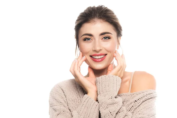 Freudige Frau in stylischem Pullover berührt Gesicht, während sie isoliert auf weiß in die Kamera schaut — Stockfoto