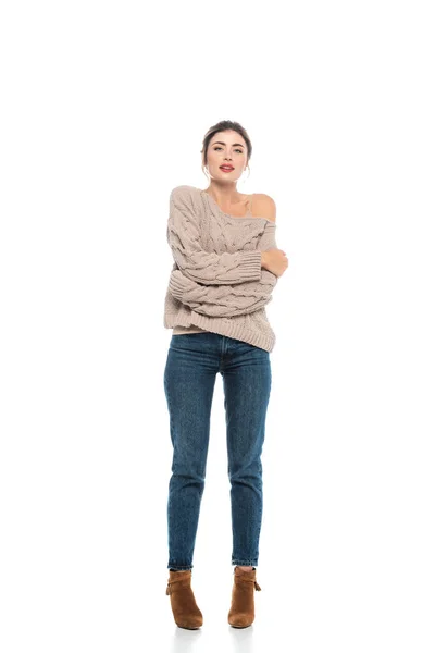 Full length view of trendy woman in openwork sweater and jeans hugging herself while posing on white — Stock Photo