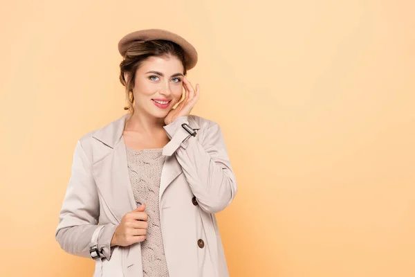 Young woman in stylish autumn outfit touching face while looking at camera on peach — Stock Photo