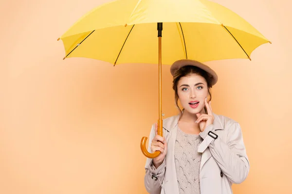 Femme élégante en tenue d'automne toucher le visage sous parapluie jaune sur la pêche — Photo de stock