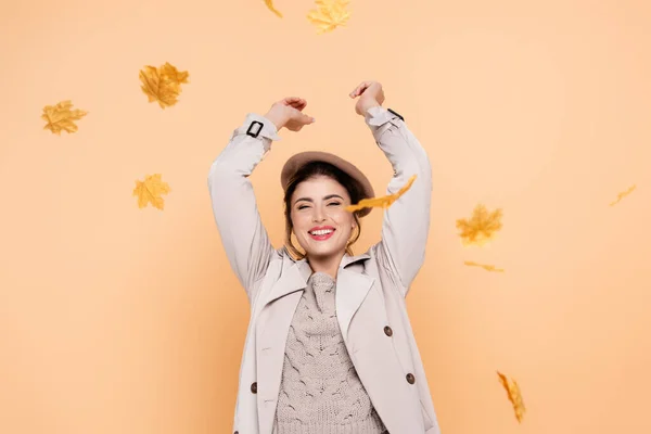 Femme excitée en trench coat et béret jetant des feuilles jaunes sur la pêche — Photo de stock