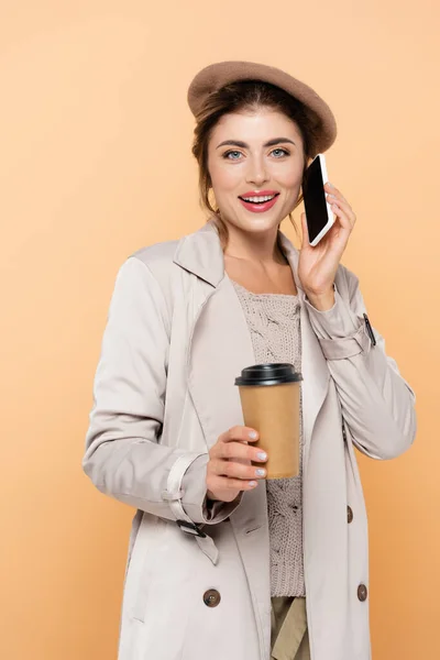 Stylische Frau im Herbst-Outfit mit Coffee to go, während sie auf dem Smartphone isoliert über Pfirsich spricht — Stockfoto