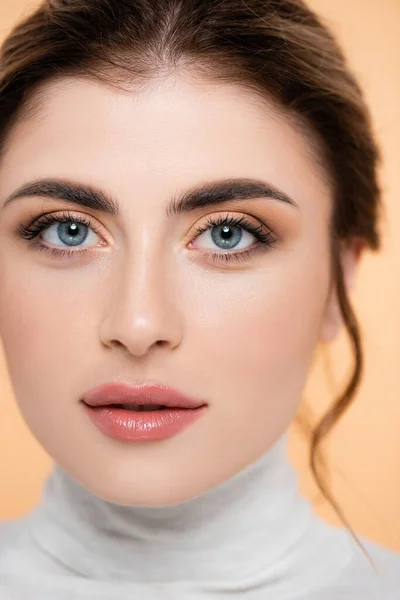 Primer plano retrato de mujer joven con maquillaje natural mirando cámara aislada en melocotón - foto de stock