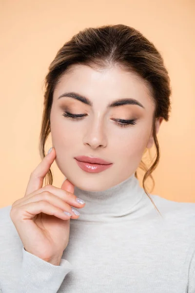 Sensual woman in turtleneck touching face isolated on peach — Stock Photo