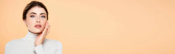 Веб-сайт заголовок стильной женщины в водолазке трогательное лицо при взгляде на камеру изолированы на персик — стоковое фото